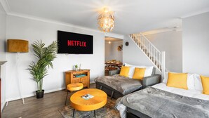 Un salon moderne doté d’un téléviseur à écran plat, d’un escalier et d’un coin repas.