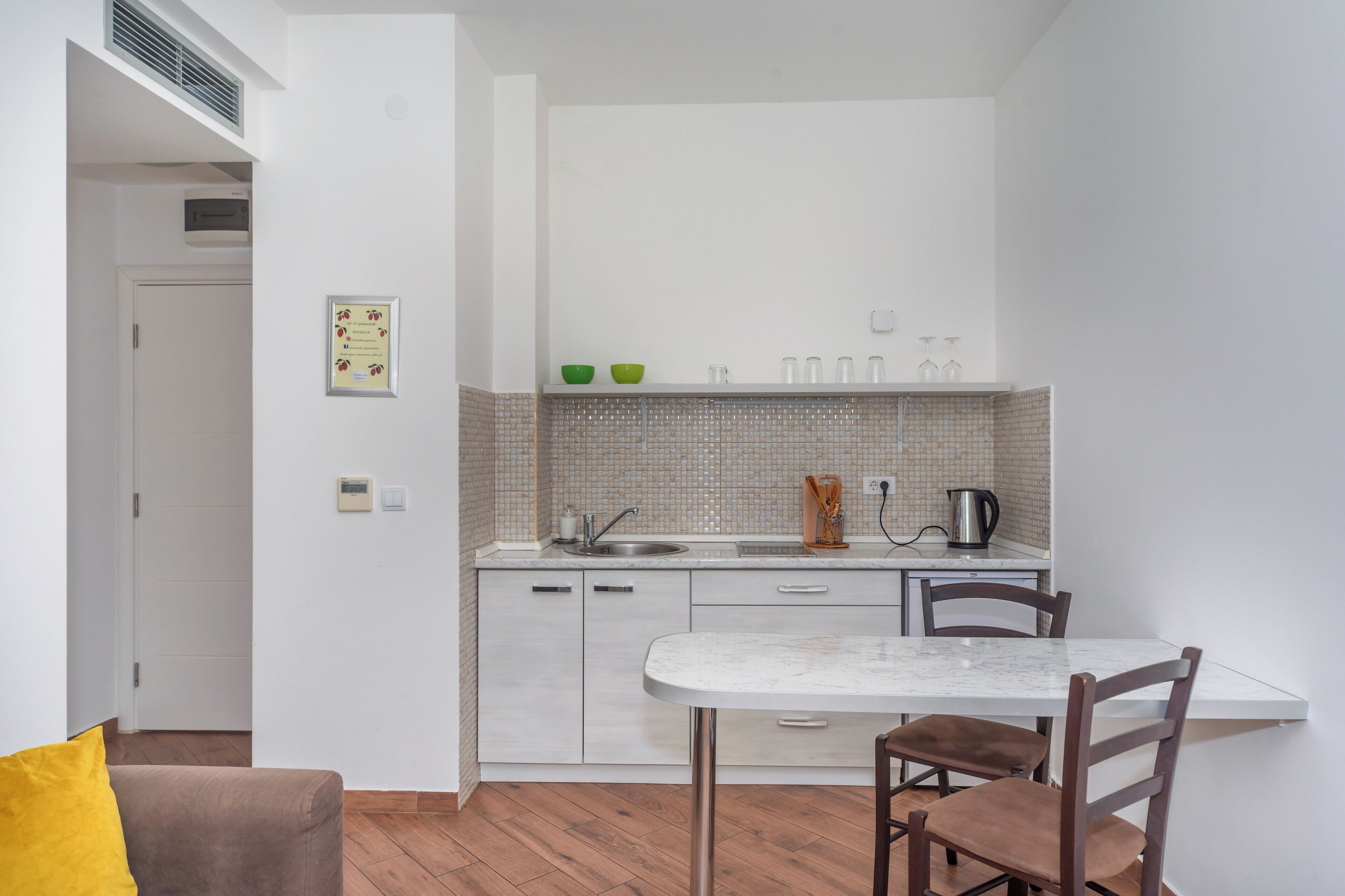 Une cuisine compacte avec des meubles blancs, un pare-feu en carrelage, un évier et un petit coin repas comprenant une table et des chaises.