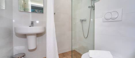 Un baño con cabina de ducha de vidrio, un lavamanos blanco y un inodoro.