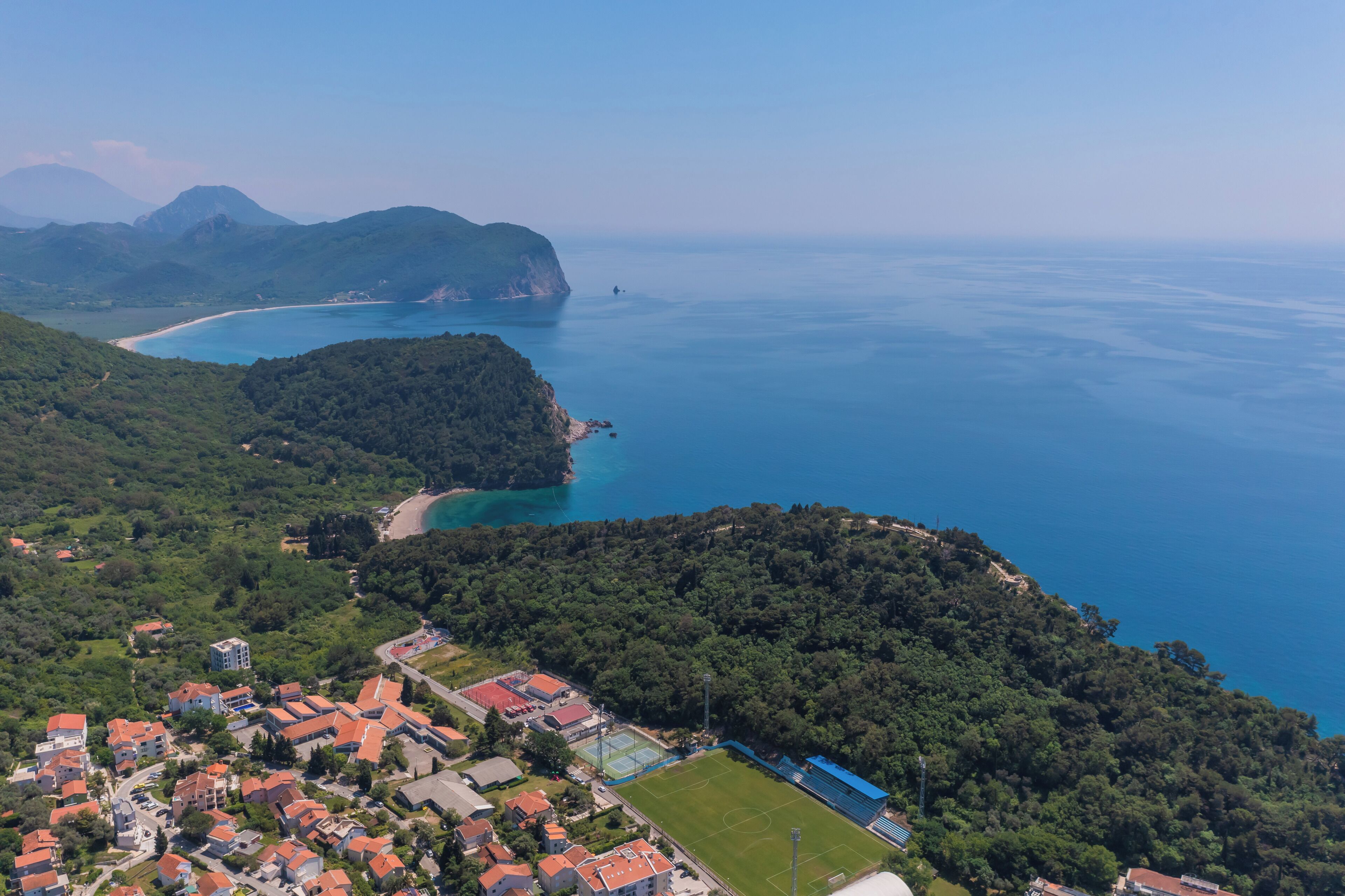 Vue aérienne d’une ville côtière, avec des immeubles résidentiels, une plage et une chaîne de montagnes en arrière-plan.