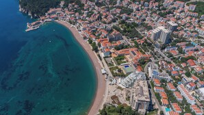 An aerial view of a coastal town with a beach, residential buildings, and a marina. - Apartments Fortunella (Petrovac)