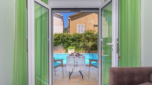 A room with a sliding glass door leading to a pool area, a sofa, and a table with chairs. - Apartments Fortunella (Petrovac)