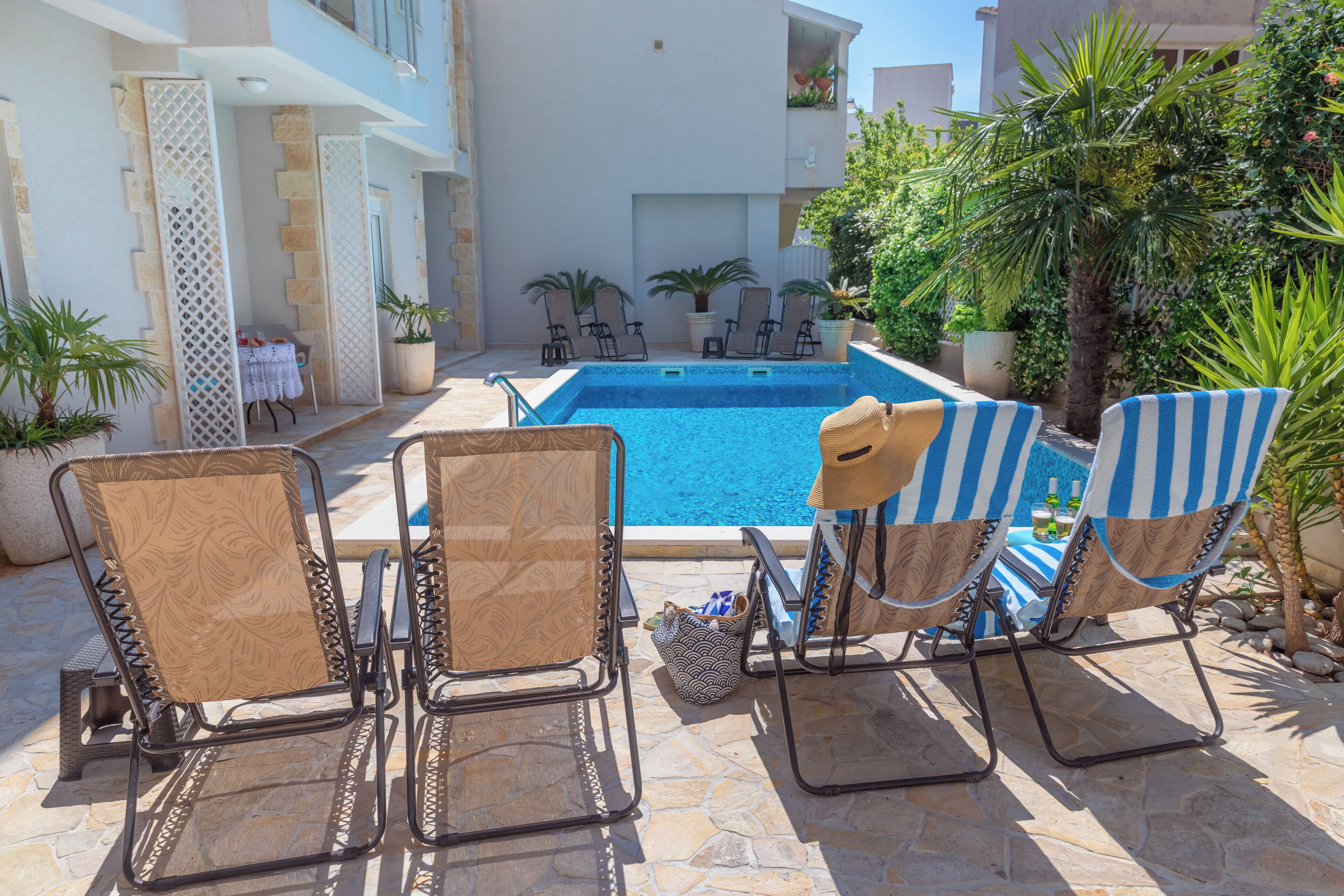 Un espace aménagé au bord de la piscine, avec des chaises longues, une table recouverte d’une nappe blanche et des plantes en pot.