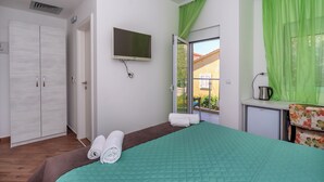 A bedroom with a bed, a TV, a desk with a kettle, and a window with green curtains. - Apartments Fortunella (Petrovac)