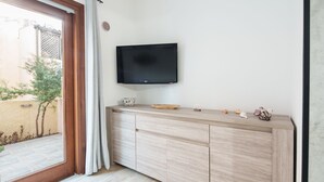 Ett modernt vardagsrum med en platt-TV som är monterad på väggen, ett träskåp med dekorativa föremål och en skjutdörr i glas som leder ut till ett utomhusområde.