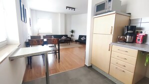 A modern kitchen with a microwave, coffee maker, and cabinets. There is a dining area with a table and chairs, and a living room with a sofa and a plant. - MuNo-Apartment | vacation apartment in Radebeul directly on the border to Dresden (Radebeul)