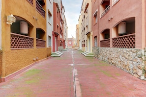 A narrow alleyway between buildings with a brick pathway, stone walls, and balconies with lattice railings.
