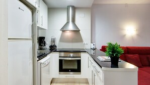 A compact kitchen with a built-in oven, a coffee maker, and a red couch in the adjacent living area.