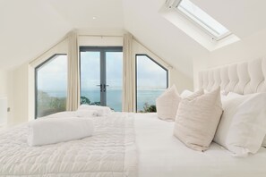 Une chambre avec un grand lit, une lucarne et une vue sur la mer.