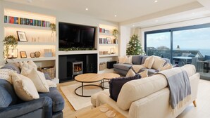 Una sala de estar moderna con chimenea, televisor de pantalla plana y un amplio ventanal con vista al mar.