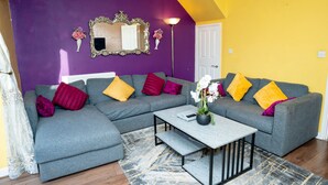 A living room with a grey sectional sofa, a small coffee table, and a mirror on the purple wall. - Beautiful Luxurious Home by LFC Stadium (Liverpool)