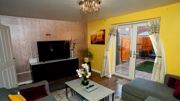 A living room with a sofa, a coffee table, a TV, and a sliding glass door leading to an outdoor area. - Beautiful Luxurious Home by LFC Stadium (Liverpool)