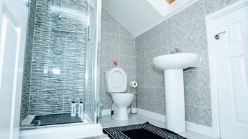 A modern bathroom with a glass shower enclosure, a toilet, a sink, and a black and white patterned rug.