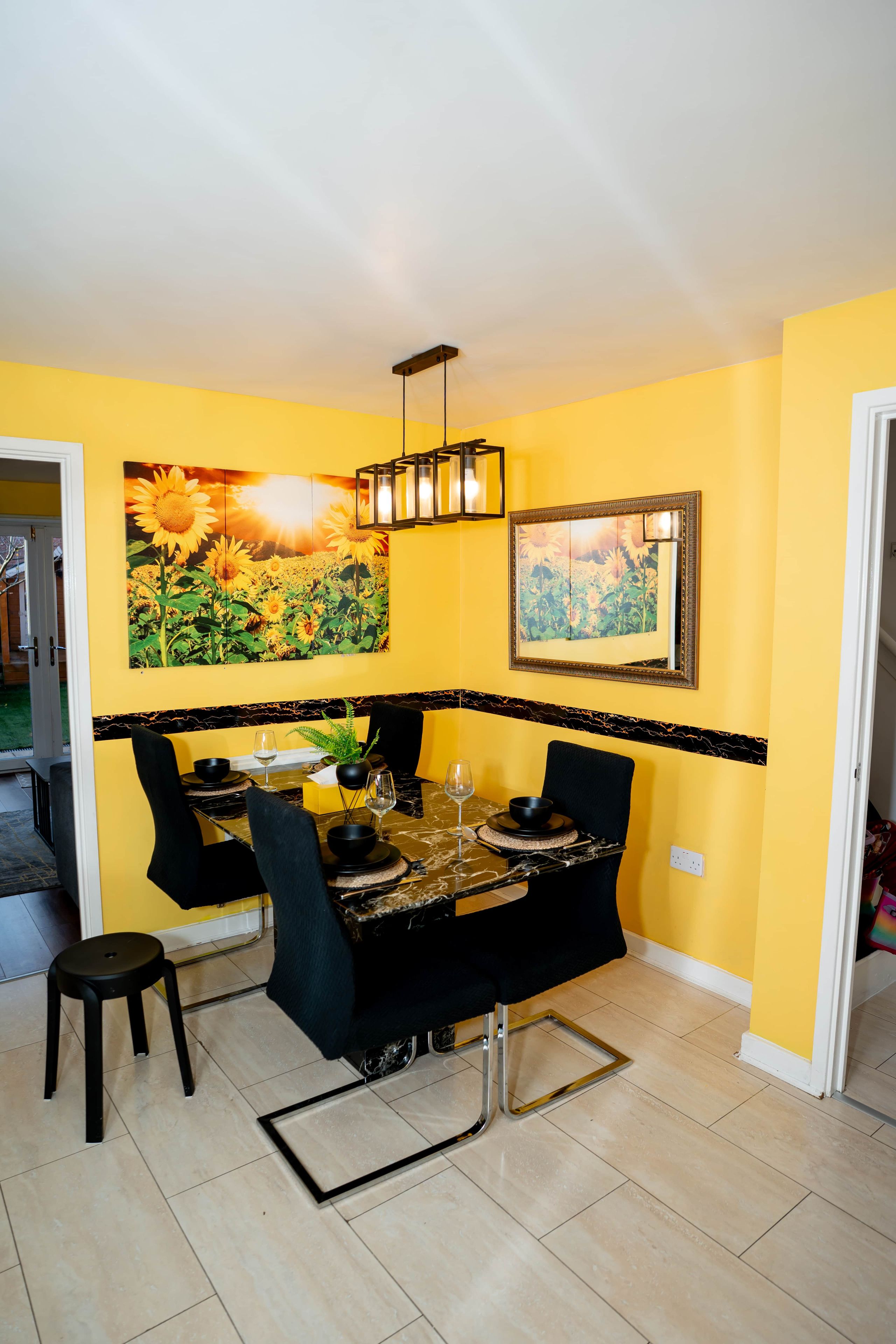 A dining area with a table set for four, chairs, a potted plant, and a wall-mounted light fixture.