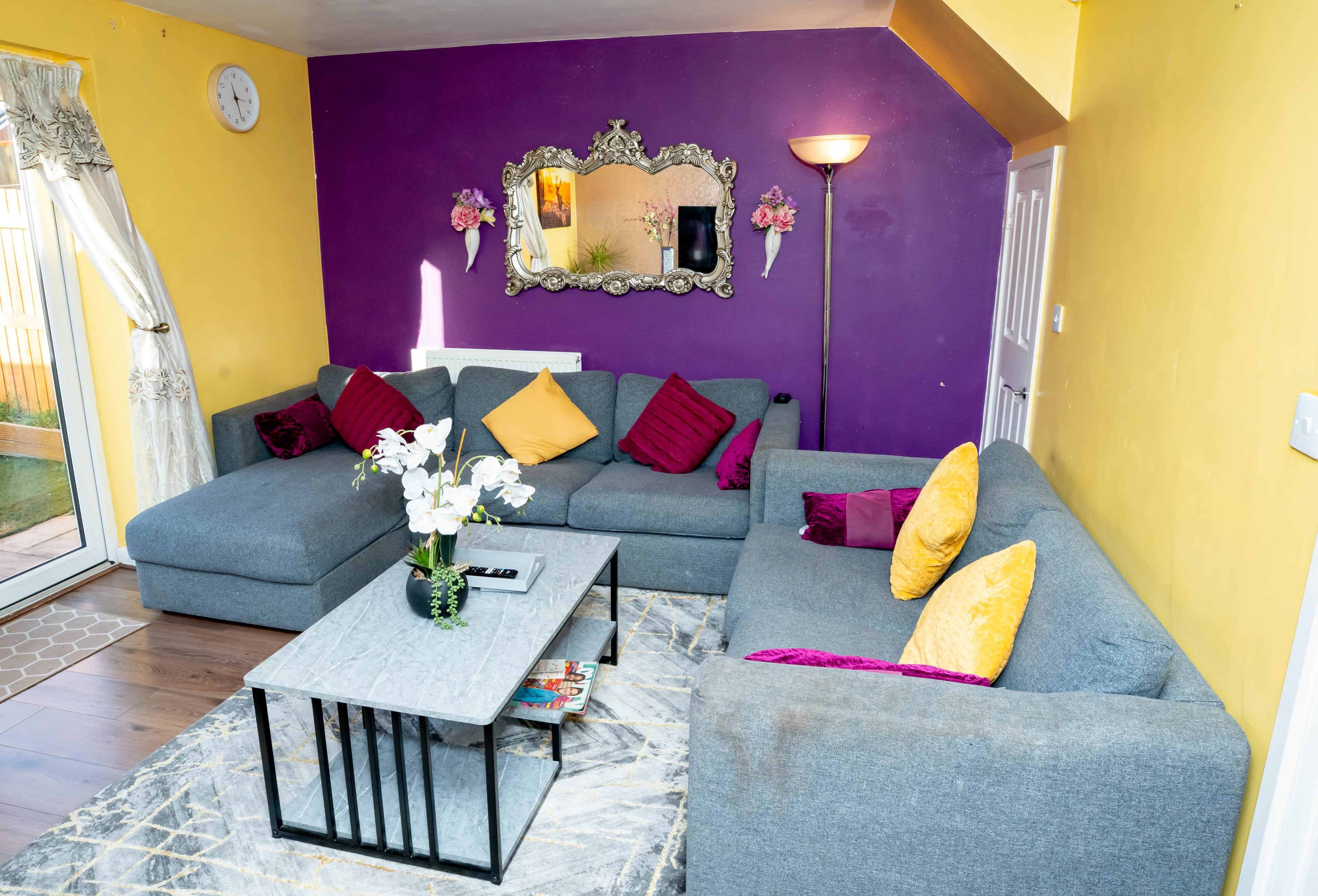 Ein Wohnzimmer mit grauem Sofa, einem Couchtisch mit Fernbedienung und einem Spiegel an der Wand.