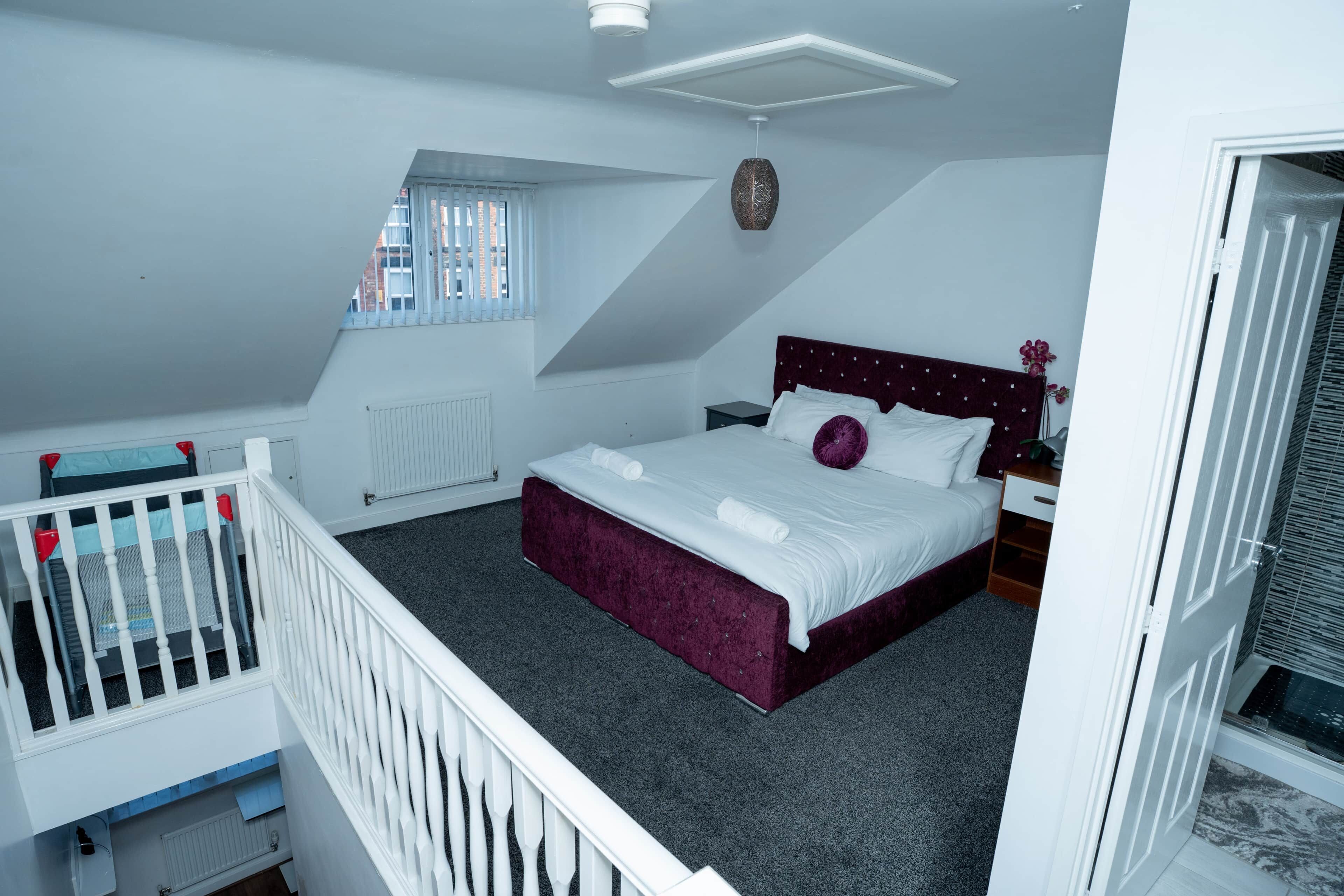 A bedroom with a bed, a window, a radiator, a white crib, and a door.