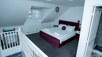 A bedroom with a bed, a window, a radiator, a white crib, and a door.