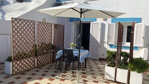 A patio with a table and chairs under a large umbrella, surrounded by a checkered floor and white walls with blue trim. - Ponzamania Sea urchin (Le Forna)