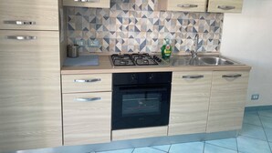 A modern kitchen with light wood cabinets, a gas stove, a built-in oven, and a patterned backsplash. - Ponzamania Sea urchin (Le Forna)
