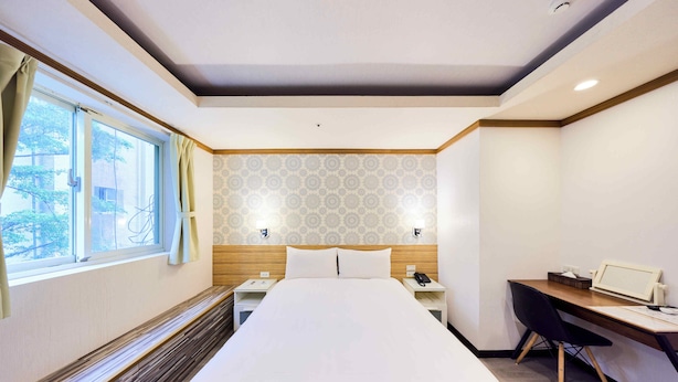 Quarto de hotel com cama, escrivaninha e janela.