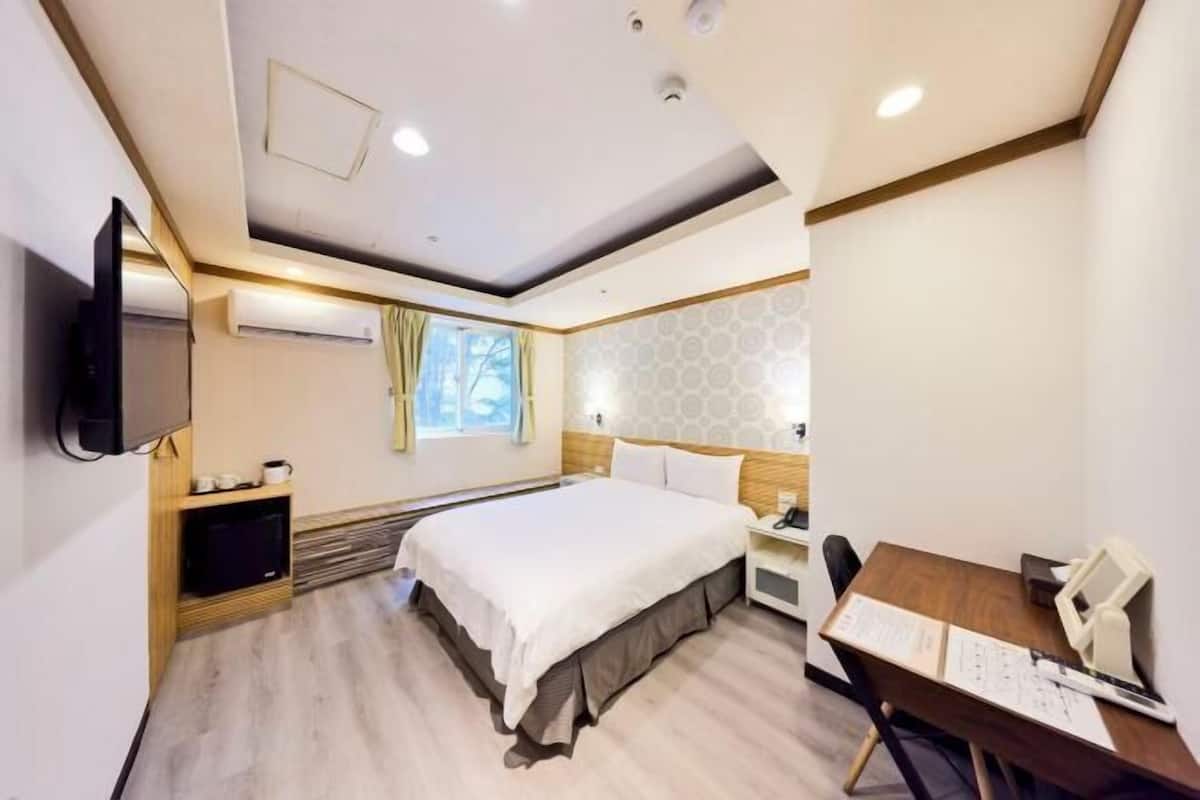 A hotel room with a bed, desk, chair, and a television.
