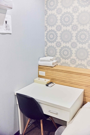 A small, neatly arranged hotel room with a white desk, a black chair, a wooden headboard, and a patterned wallpaper. - Travel Time Hotel (Taipei)