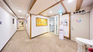 Um corredor com piso estampado, um quadro emoldurado, uma porta com painel de vidro e um balcão branco com pia.