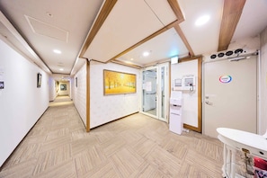 A hallway with patterned flooring, a framed painting, a door with a glass panel, and a white counter with a sink. - Travel Time Hotel (Taipei)