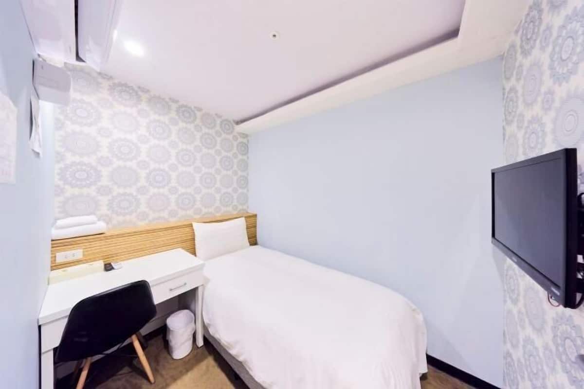 A hotel room with a bed, desk, chair, and a TV mounted on the wall.