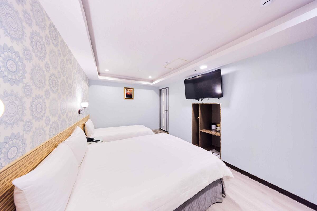 A hotel room with two beds, a television, a wardrobe, and a patterned wall.
