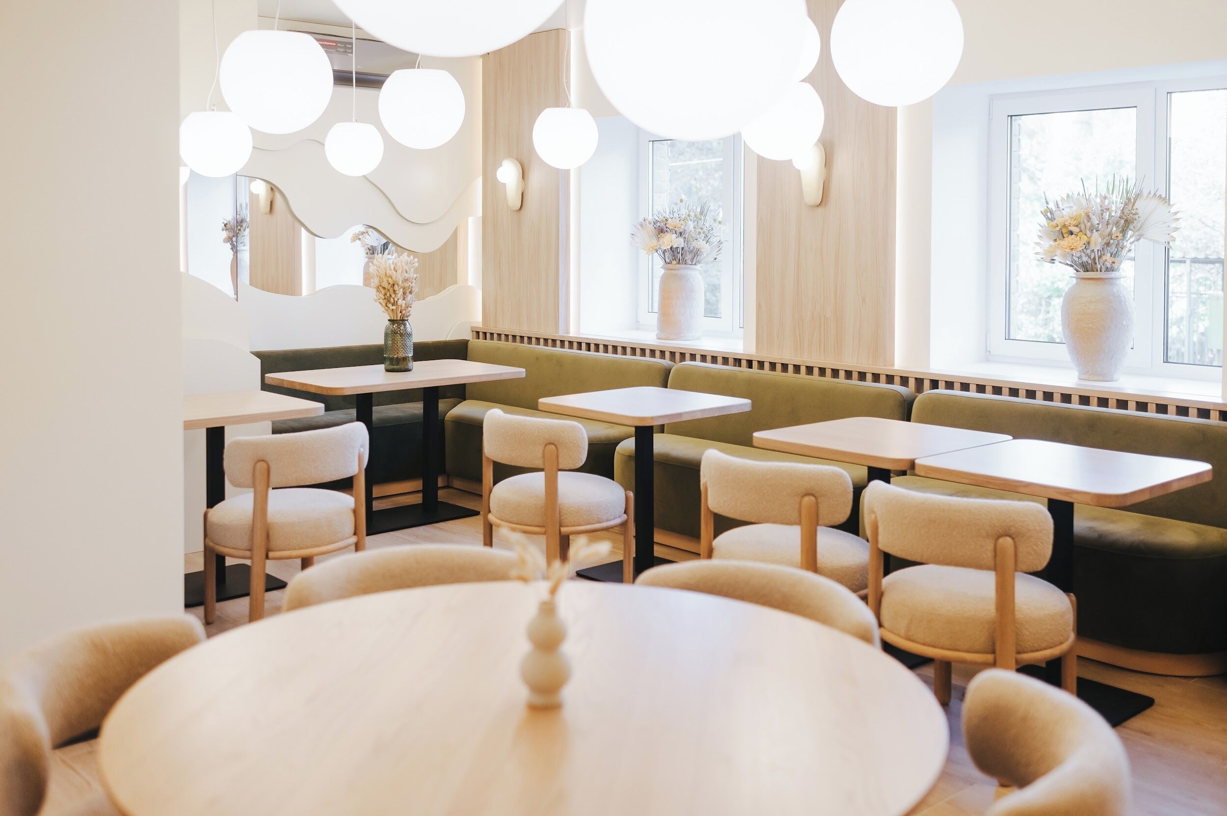 A modern dining area with round tables and cushioned chairs, wooden accents, and large windows with natural light.