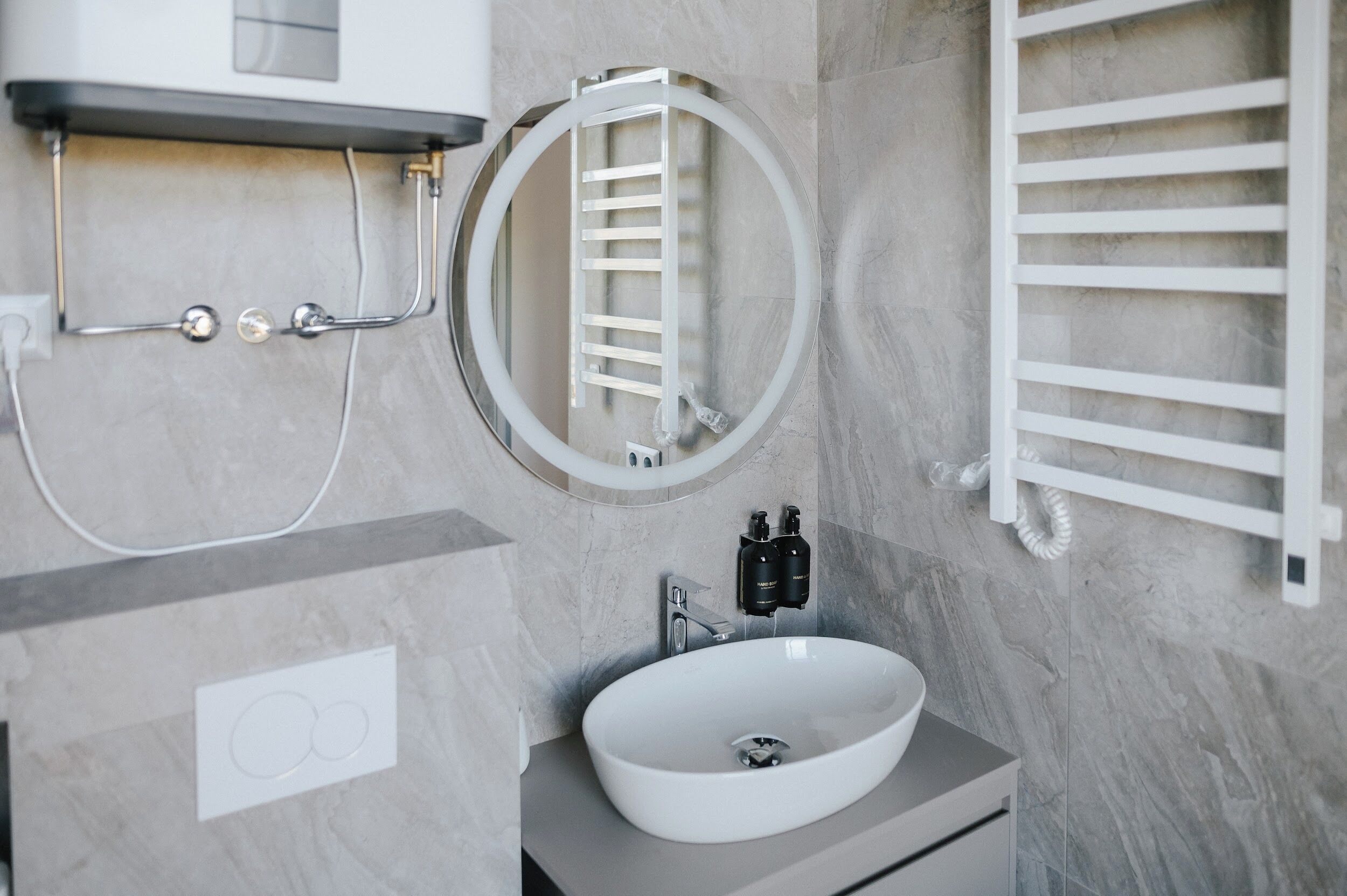 A modern bathroom with a round mirror, a white sink, and a towel rack.