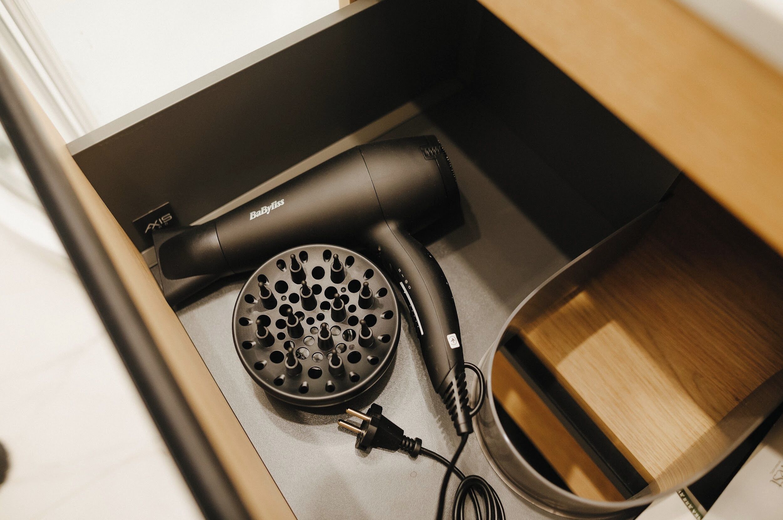 A black hair dryer and a plug in a drawer.