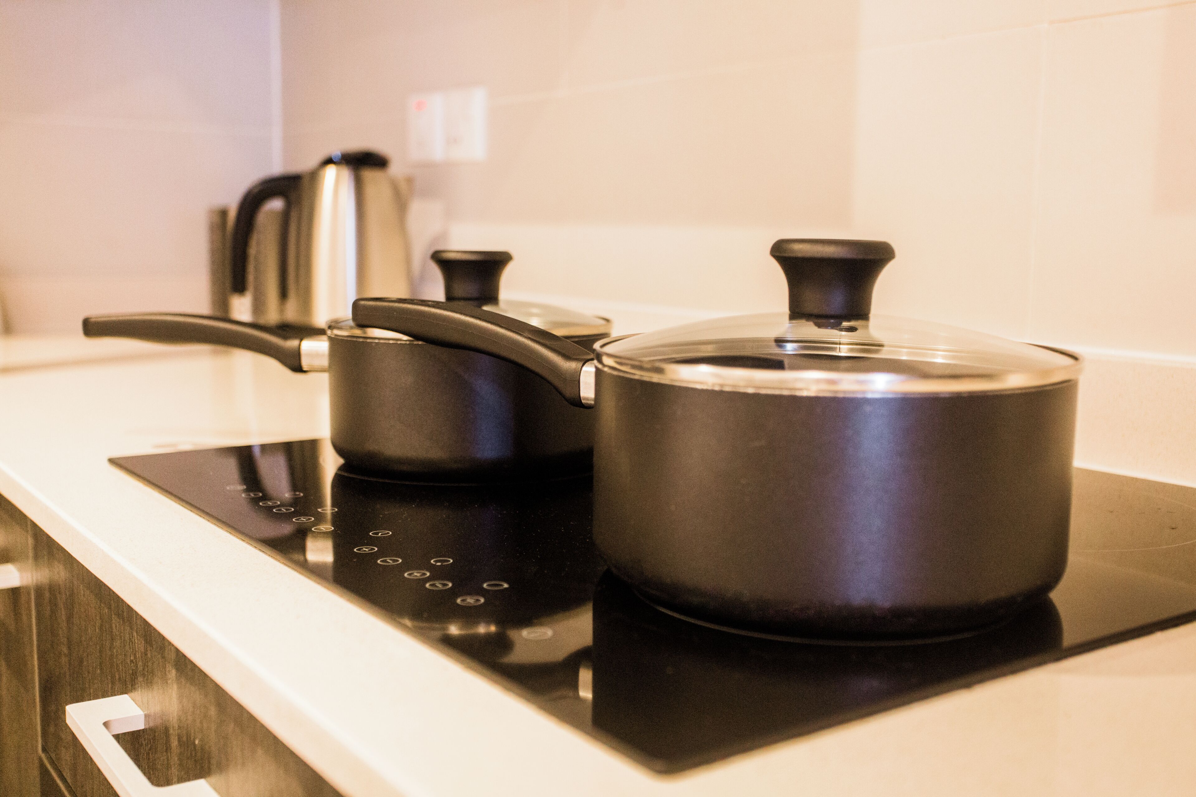 Una cocina con tope de inducción negro, una olla y un hervidor.