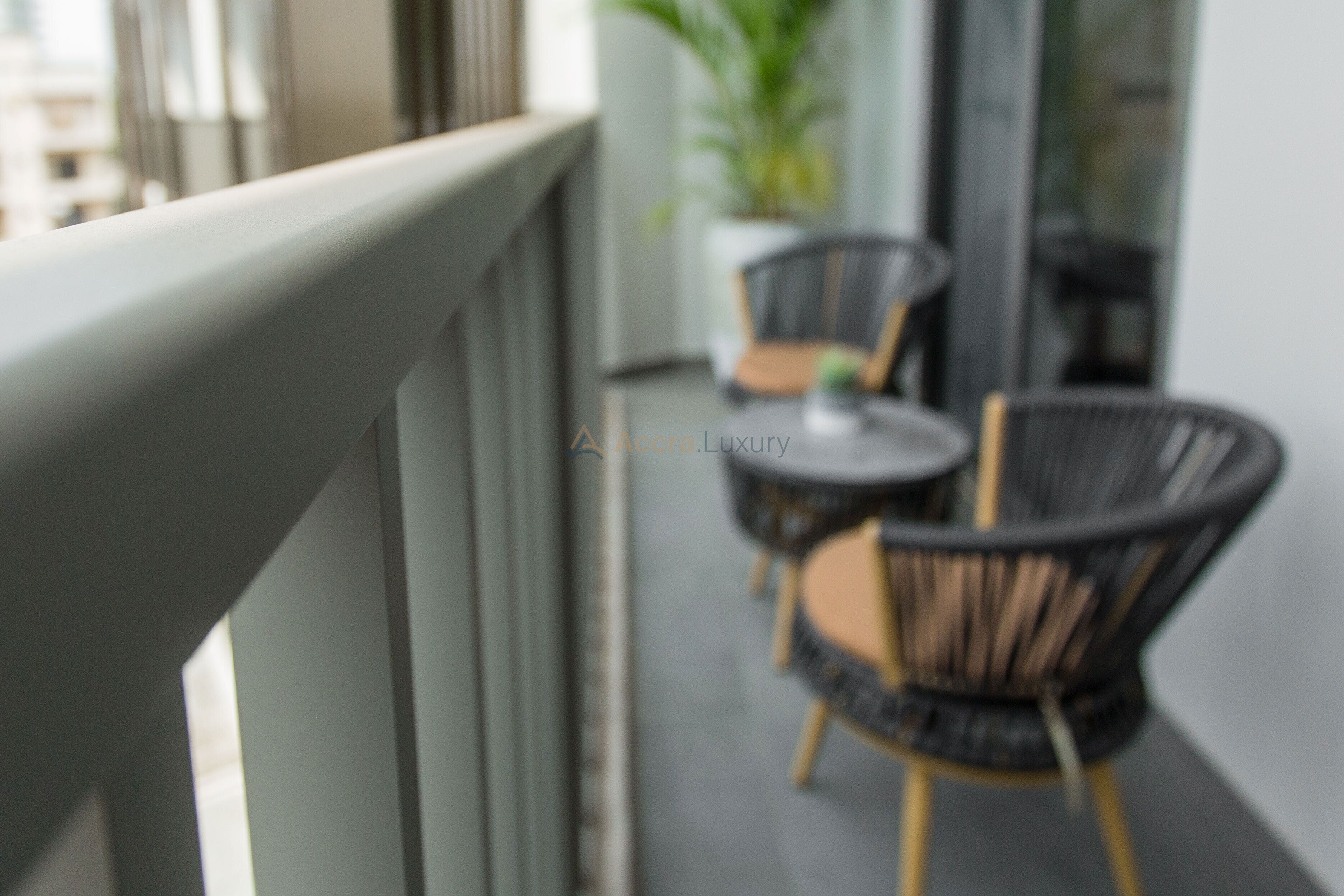 A balcony with wicker chairs and a small table, a potted plant, and a view of the city.