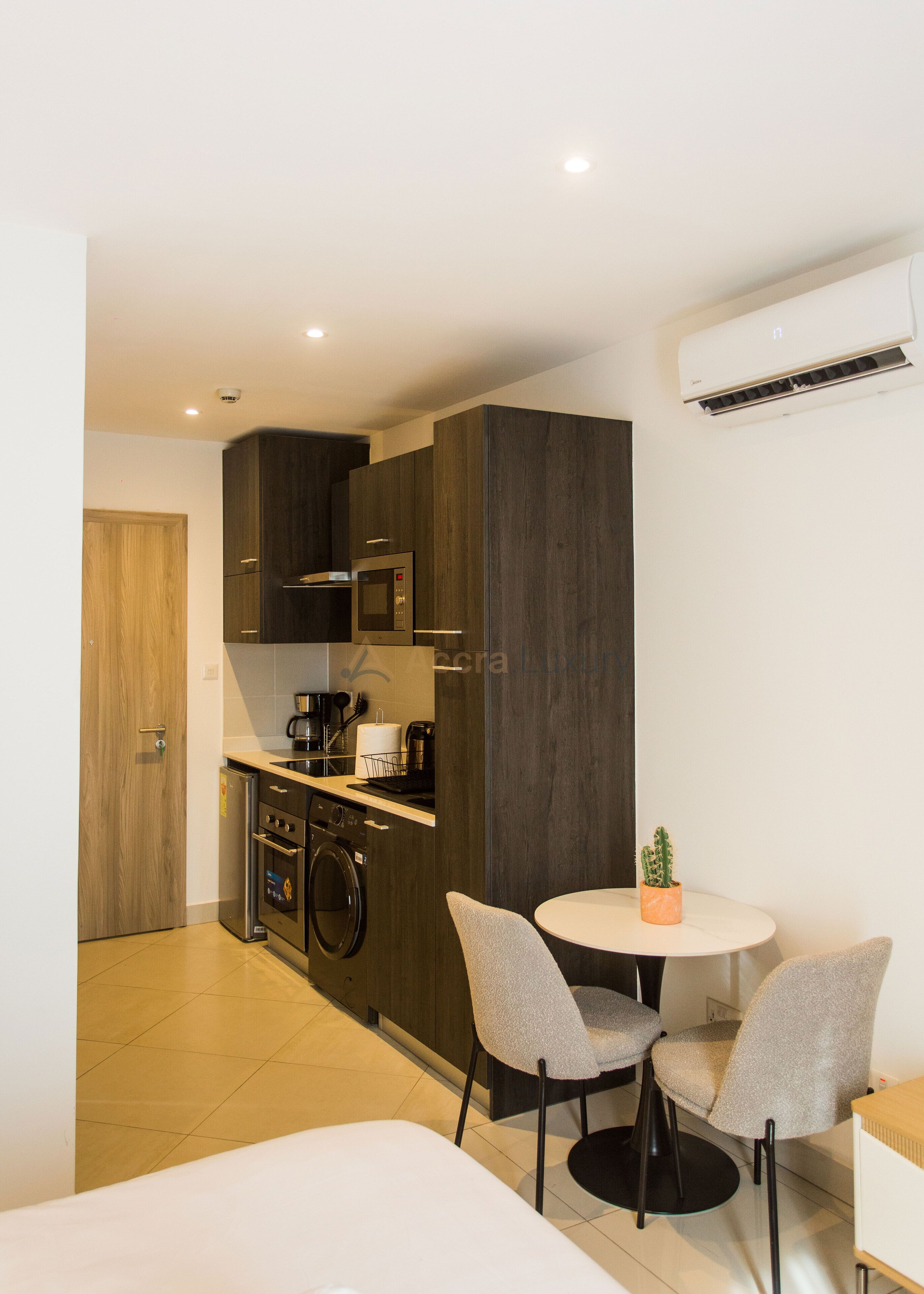 A compact kitchen with modern appliances, a dining area with two chairs, and a small table with a potted plant.