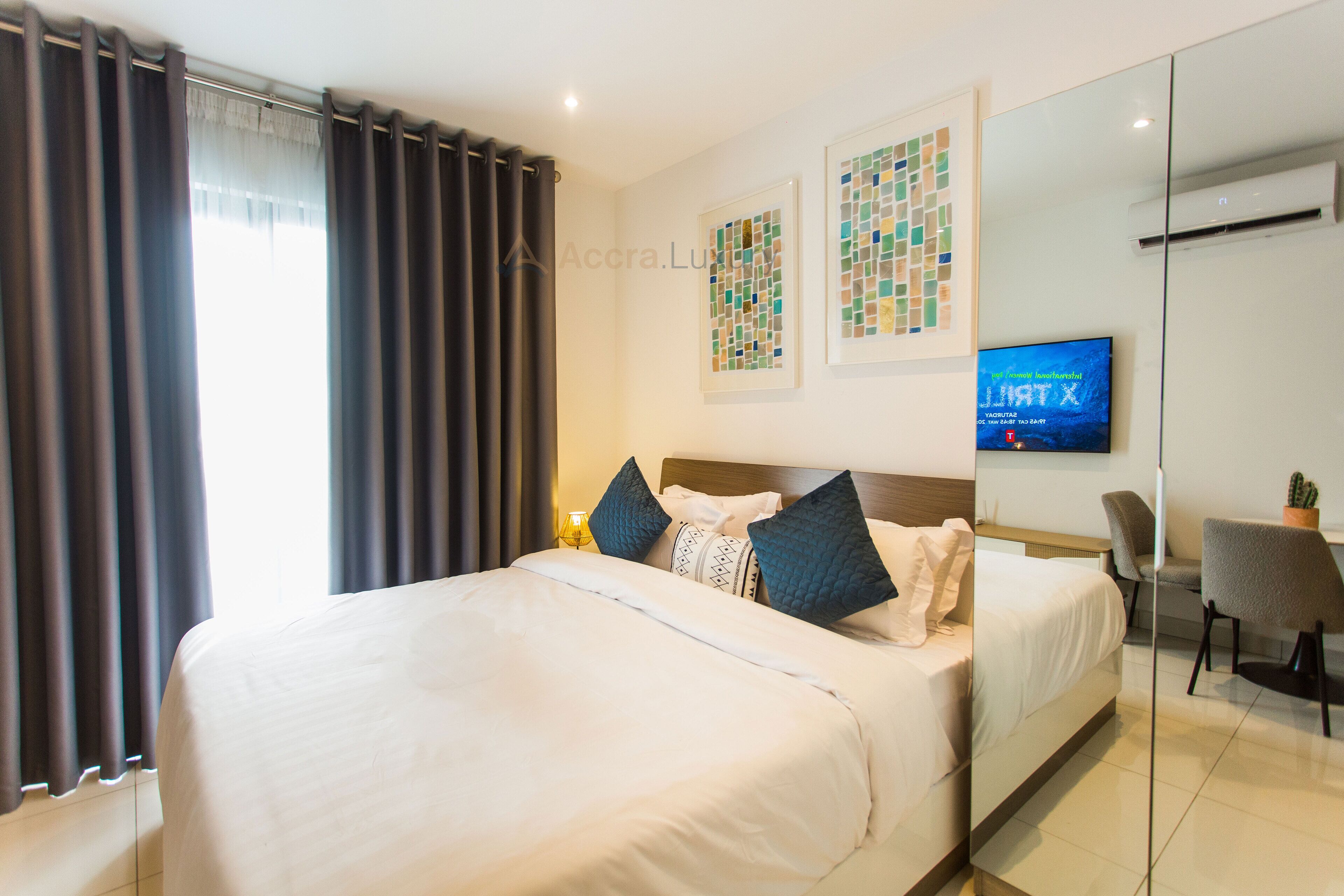 A hotel room with a large bed, a desk, a chair, and a TV on the wall.