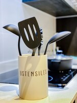 A kitchen utensil holder with the word "USTENSILES" on it, placed on a countertop.