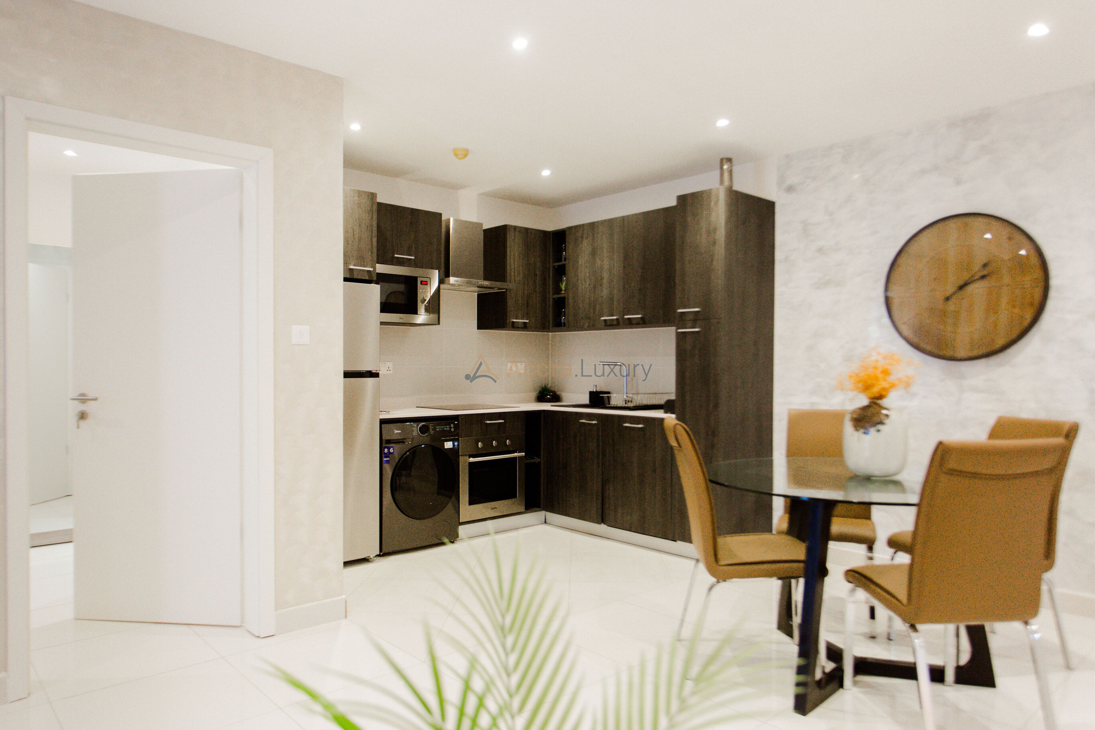 Una cocina moderna con armarios de madera oscura, electrodomésticos de acero inoxidable y una mesa de vidrio con dos sillas.