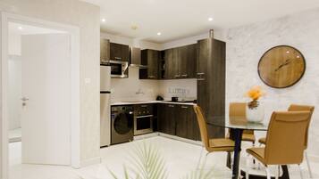 Una cocina moderna con armarios de madera oscura, electrodomésticos de acero inoxidable y una mesa de vidrio con dos sillas.