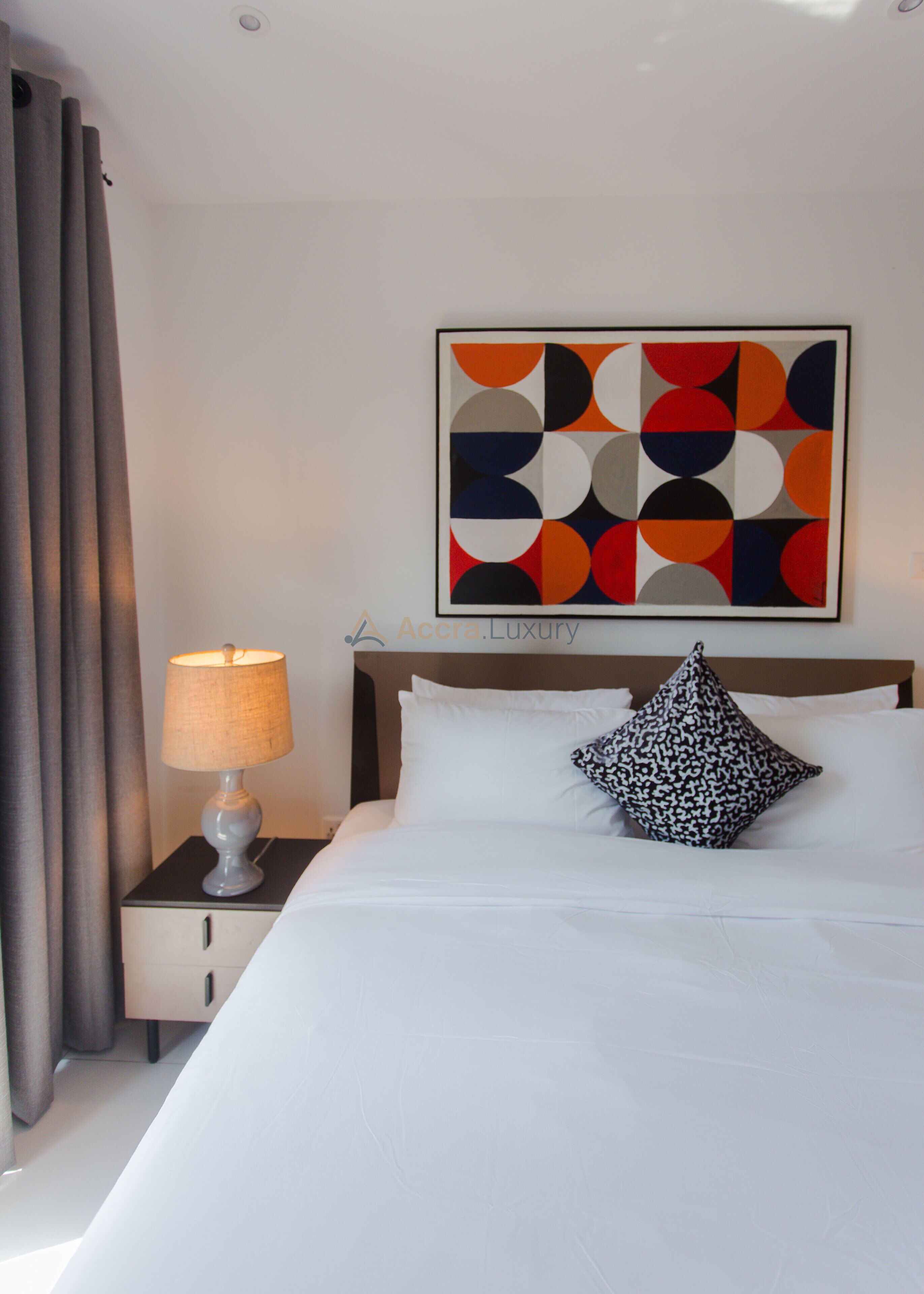 Quarto de hotel com cama, mesa de cabeceira com luminária, travesseiro e uma obra de arte na parede.
