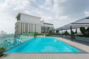 Una piscina moderna en la azotea con barandilla de cristal, rodeada de una terraza de madera y vegetación.