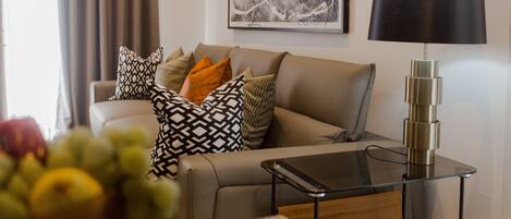 A living room with a sofa, patterned cushions, a glass coffee table, and a modern floor lamp.