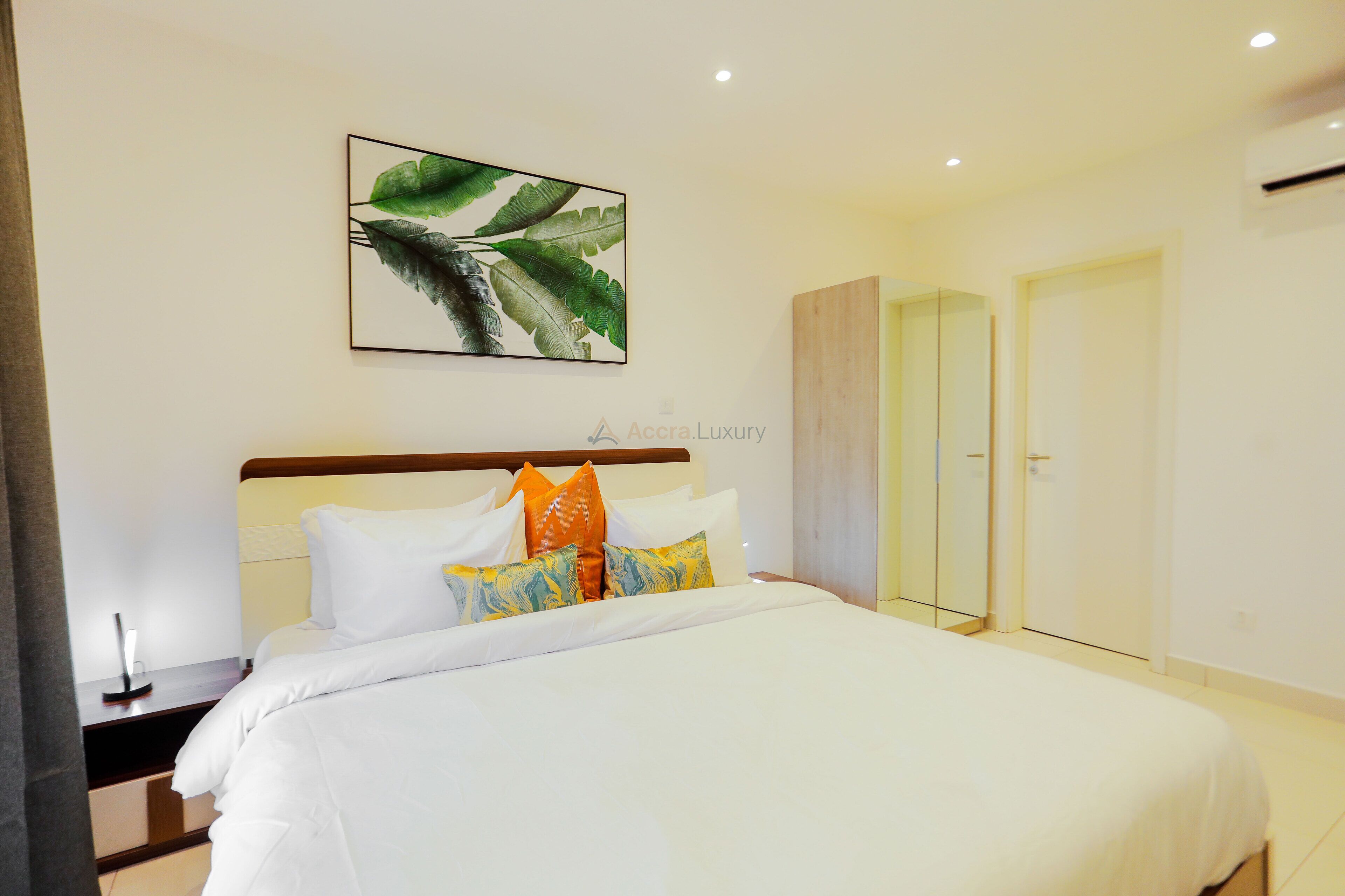 A hotel room with a neatly made bed, a large mirror, and a framed artwork on the wall.