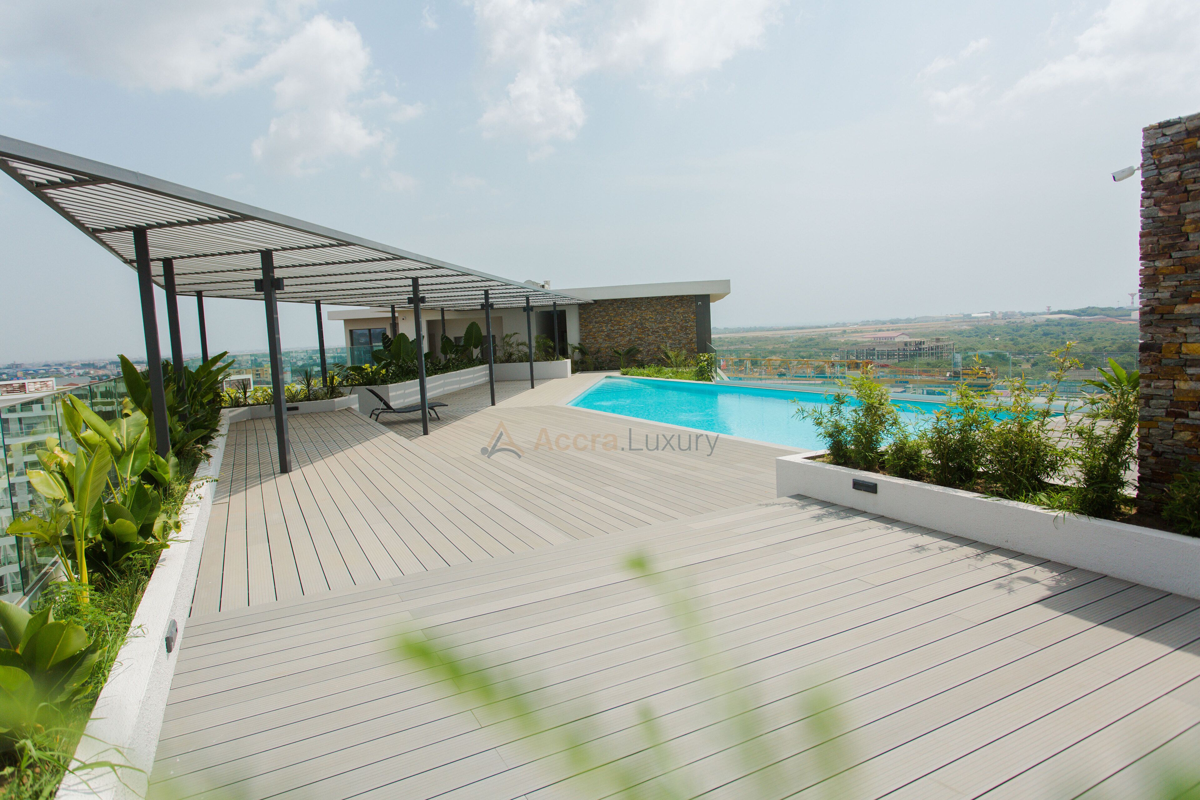 Un área de piscina en la azotea con un pérgola, un pequeño edificio y vistas de la ciudad.