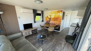 A modern living room with a sofa, a TV, a dining table with chairs, and a mural of a deer.