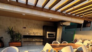 Un espace de restauration en plein air avec une table en bois et des chaises modernes, un four encastré et des plantes en pot.