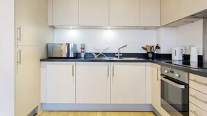 Une cuisine moderne avec des meubles blancs, un plan de travail noir, un évier en acier inoxydable et un four.