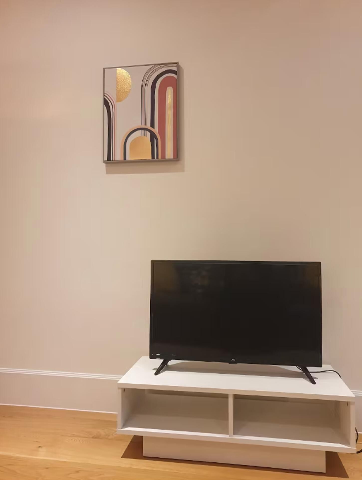 A flat-screen TV on a white stand in a room with a plain wall and a wooden floor.