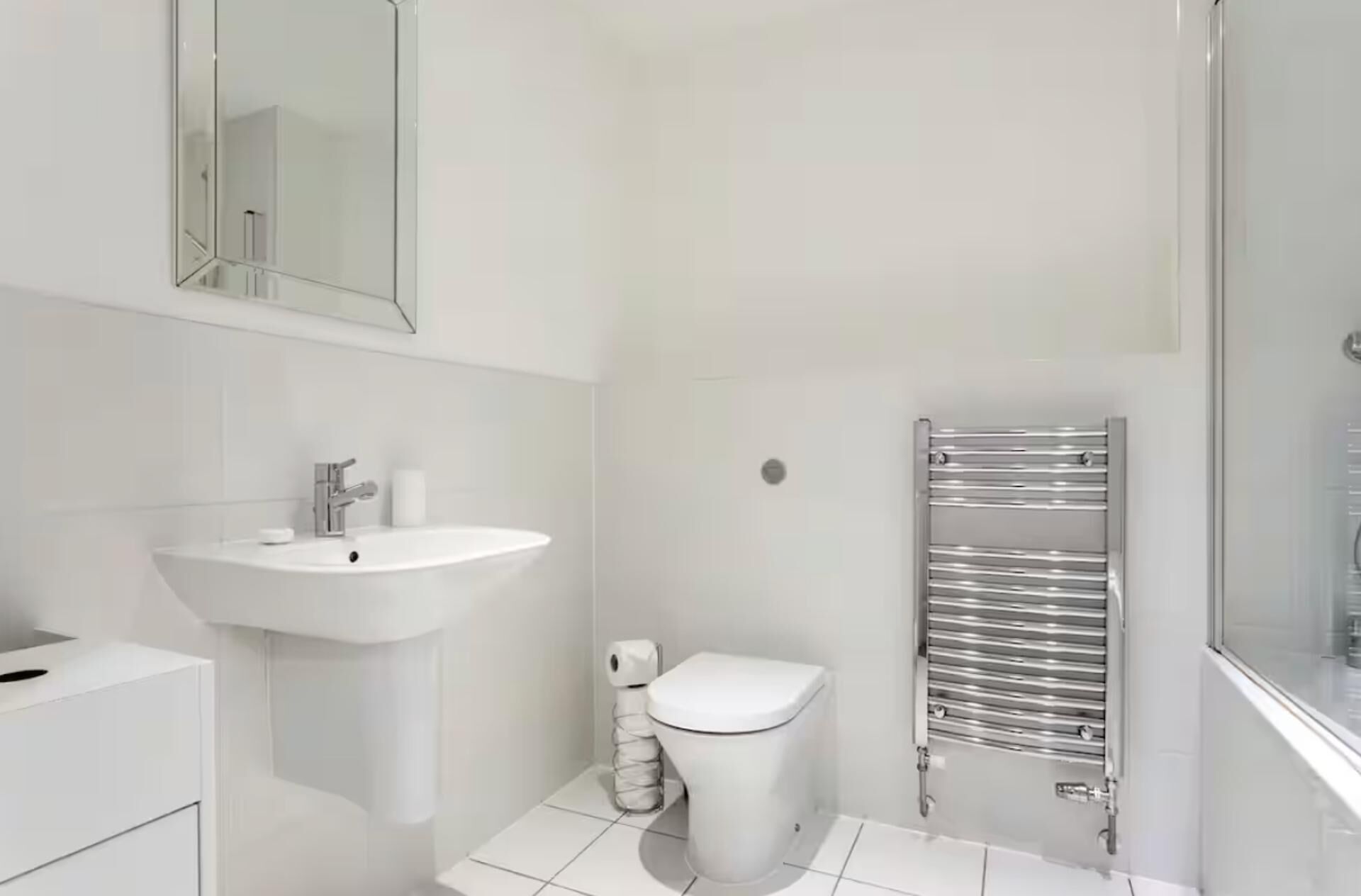 A modern bathroom with a white sink, toilet, and a chrome towel rail.